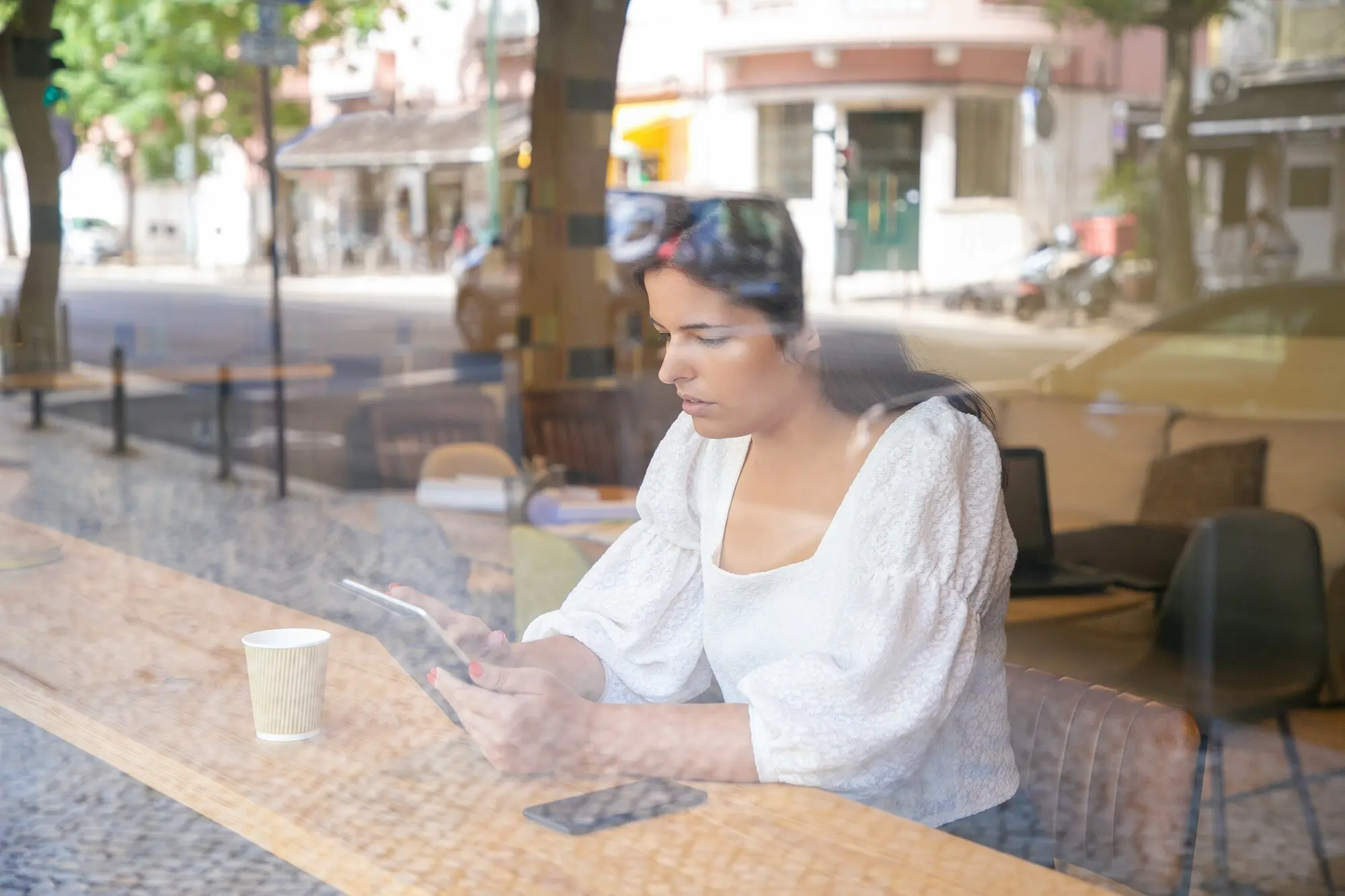 Nachdenkliche junge Geschäftsfrau sitzt an einem Schreibtisch in einem Coworking-Space oder Café und benutzt ein Tablet, praxisnah und nachvollziehbar.